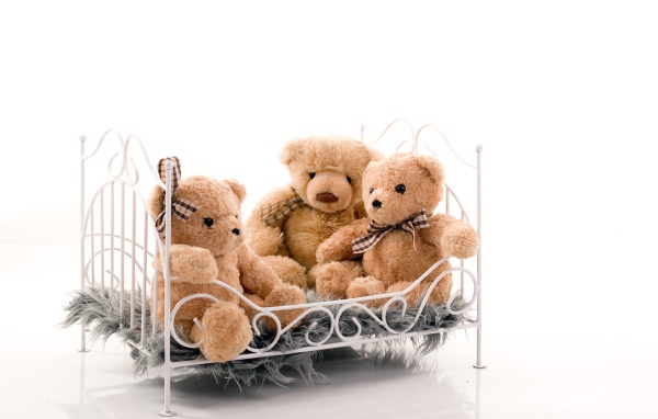 Три игрушечных медведя на кровати на белом фоне