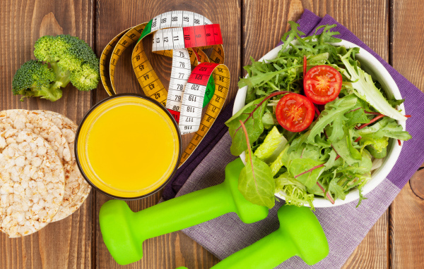 Салат из зелени на столе с соком и гантелями