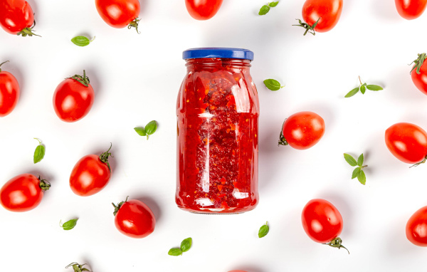 Банка аджики на белом фоне с помидорами