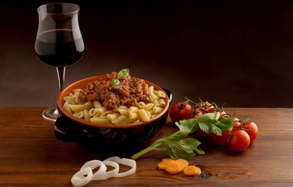 Макароны с фаршем на столе с бокалом вина и помидорами