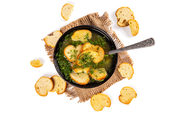 Суп с гренками и зеленью на столе на белом фоне