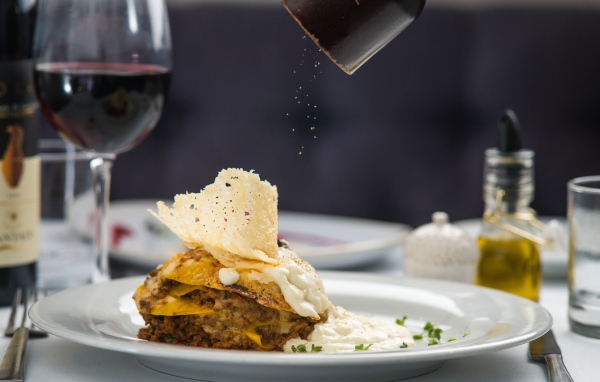 Кусок лазаньи посыпают перцем 