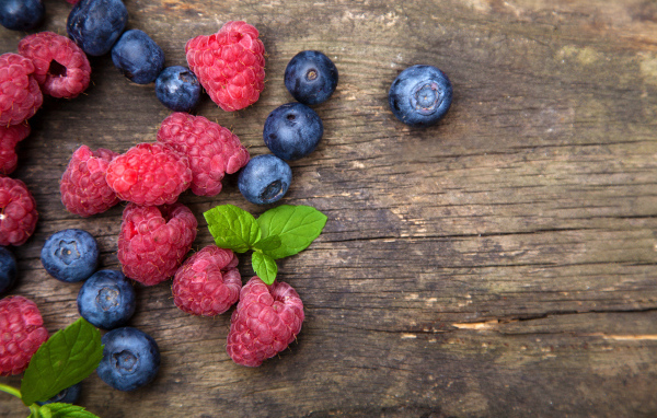 Голубые ягоды черники и красные ягоды малины на деревянном столе