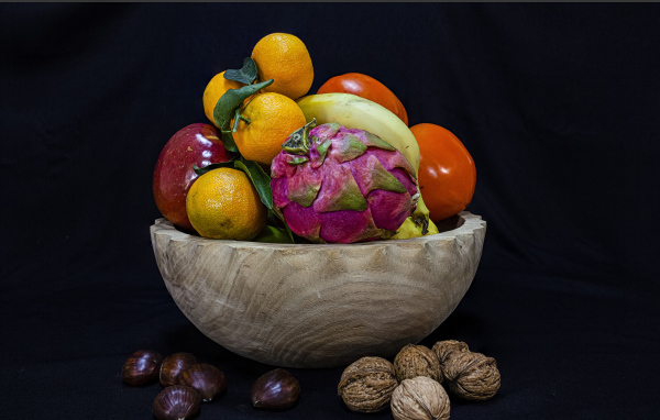 Цитрусовые фрукты в деревянной миске на черном фоне