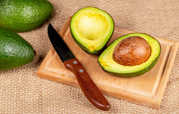 Зеленое авокадо с ножом на разделочной доске