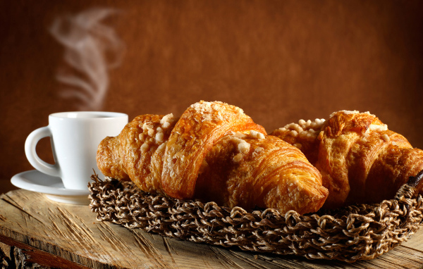 Два свежих круассана на столе с кофе 