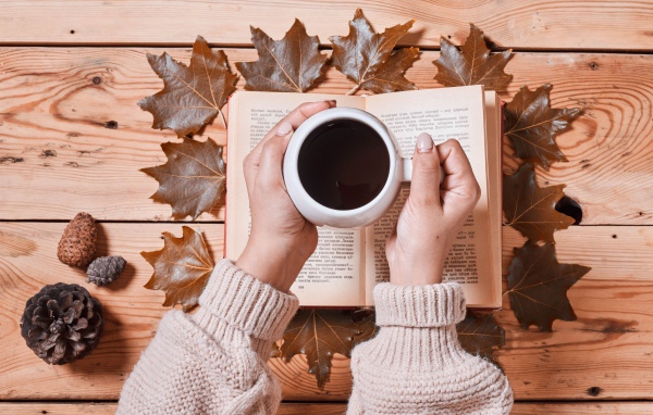 Чашка кофе в руках на столе с книгой и листьями