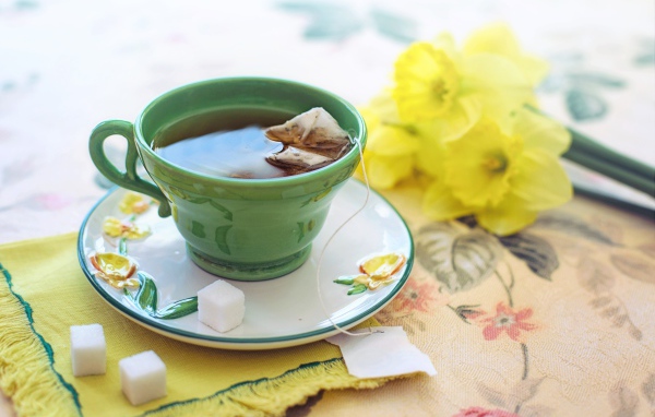 Чашка чая на столе с сахаром и нарциссами