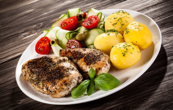 Куски курицы на тарелке с картофелем, помидорами и кабачком 