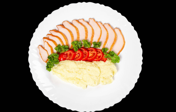 Ham on a large white plate with potatoes and tomatoes