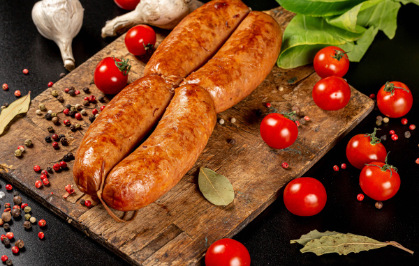 Мясные колбаски на доске с овощами