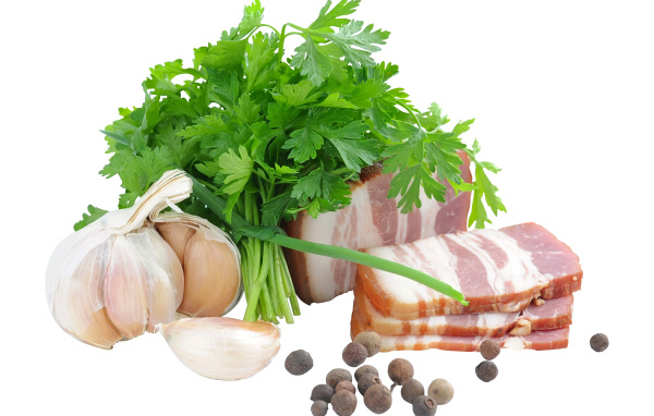 Кусок сала на белом фоне с зеленью петрушки и специями