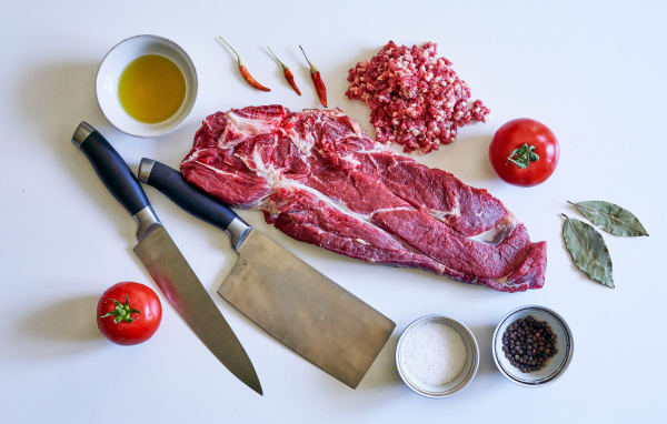 Кусок мяса со специями и ножами на столе 