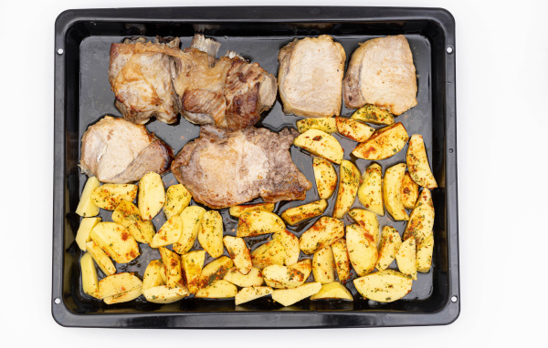 Pork on a baking sheet with potatoes on a white plate