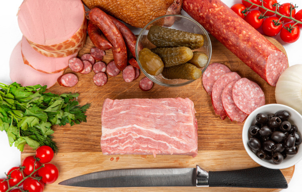 Колбаса на столе с огурцами, помидорами и зеленью 