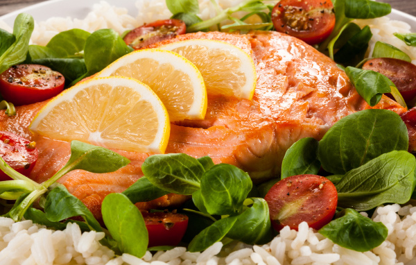 Кусок запеченной красной рыбы на тарелке с лимоном, рисом, базиликом и помидорами