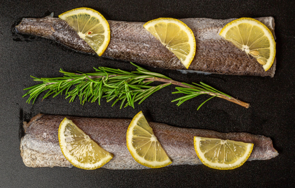 Свежее филе рыбы с лимоном и розмарином на черном фоне
