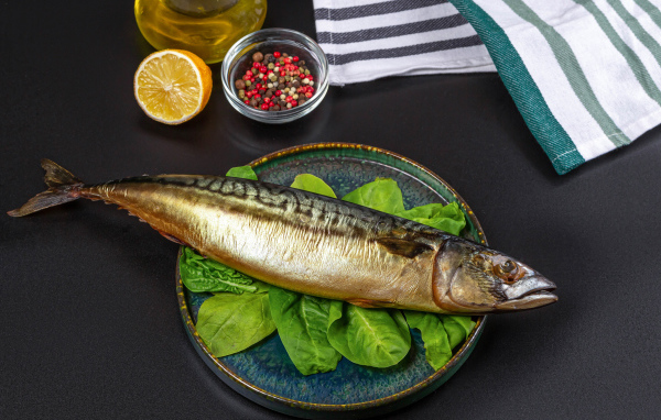Большая копченая скумбрия на тарелке с базиликом