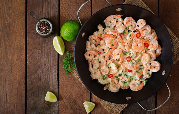 Креветки с соусом в сковороде на столе с лаймом