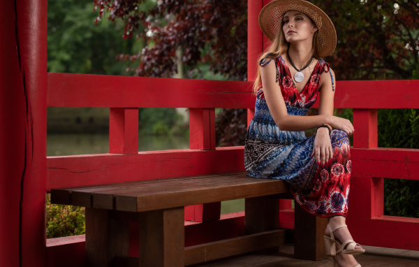 Молодая девушка в платье сидит на лавке 