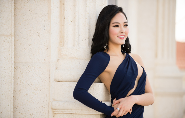 Молодая девушка в платье стоит у стены 