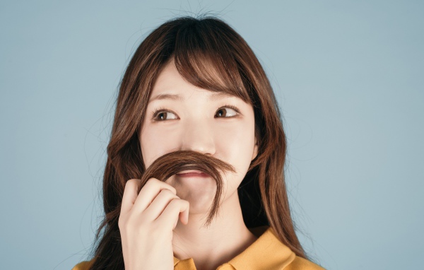 Девушка азиатка закрыла лицо волосами на сером фоне 