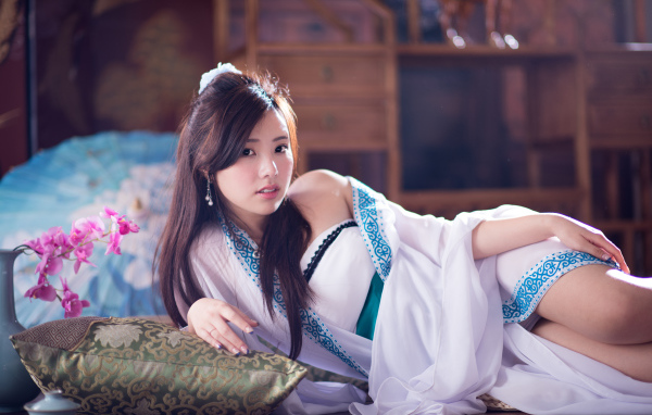 Девушка азиатка в красивом платье лежит на кровати 