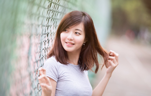 Девушка азиатка с милой улыбкой стоит у сетки 