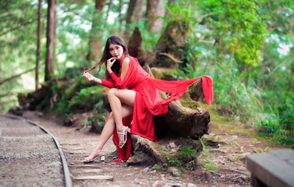 Красивая азиатка в красном платье сидит на дереве 