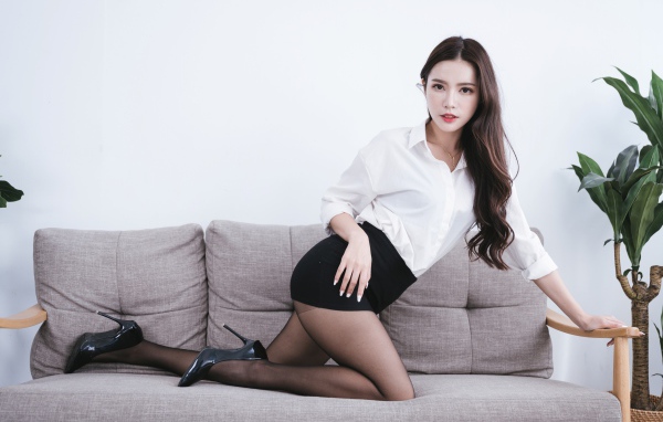 Красивая азиатка в белой рубашке на диване