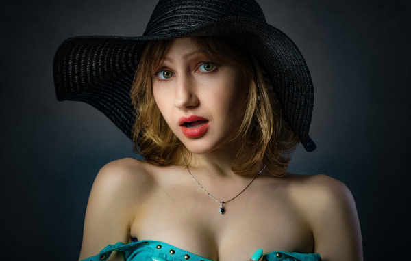 Красивая девушка в большой черной шляпе на сером фоне 