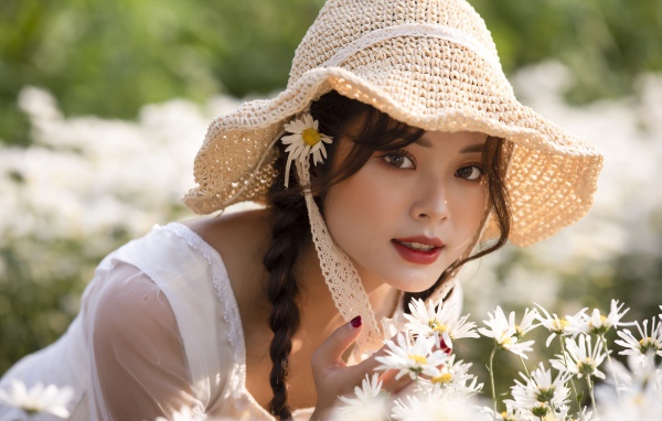Красивая девушка в шляпе на поле с ромашками 