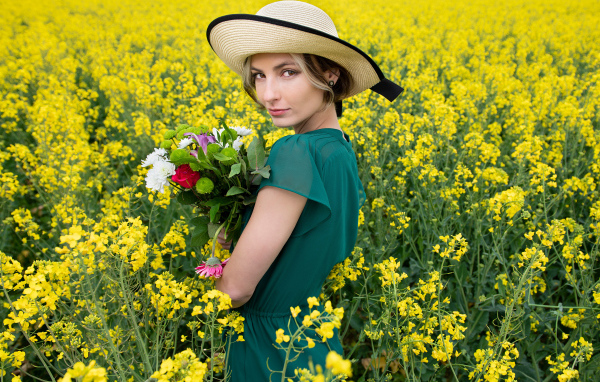 Красивая девушка в шляпе на поле с желтыми цветами летом