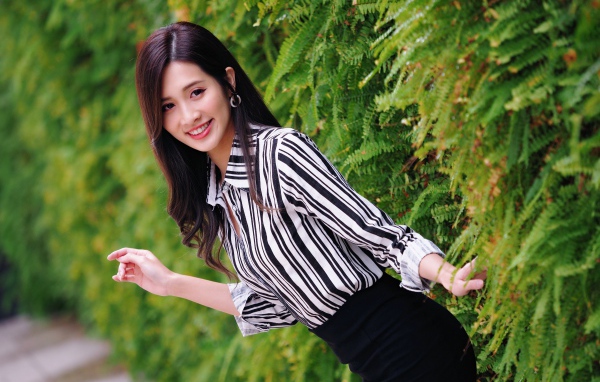 Красивая девушка в полосатой рубашке стоит у растения