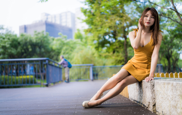 Красивая девушка в желтом платье сидит в парке 