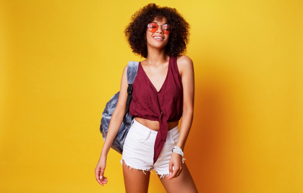 Красивая девушка в очках с рюкзаком на желтом фоне 