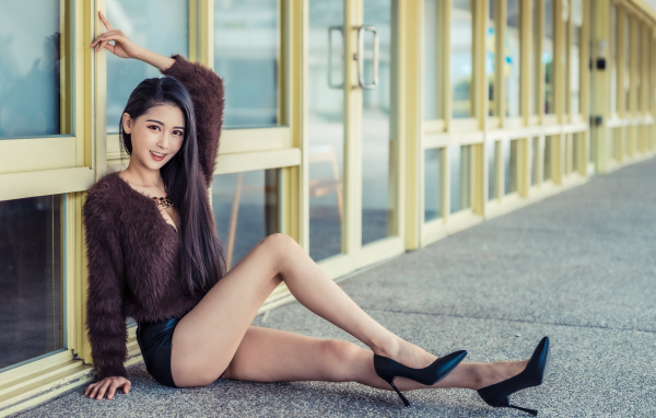 Девушка в свитере сидит у стеклянной стены 