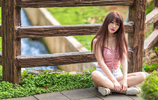 Длинноволосая азиатка сидит у забора 