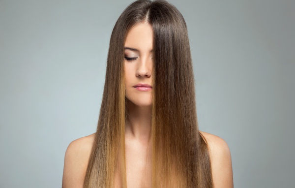 Длинноволосая шатенка с закрытыми глазами на сером фоне 