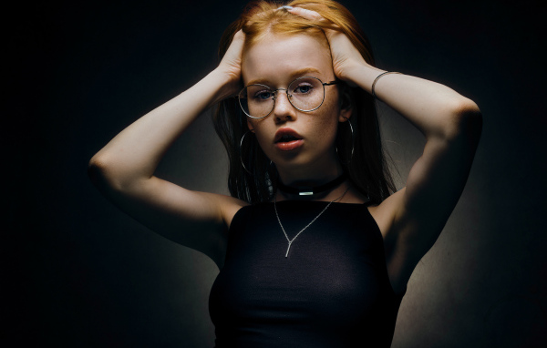 Рыжеволосая девушка в очках на черном фоне