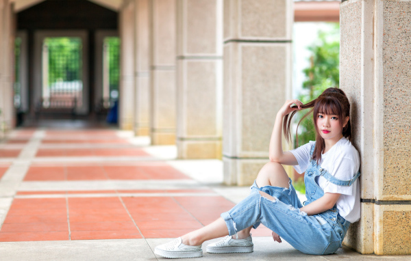 Грустная девушка азиатка сидит у колонны