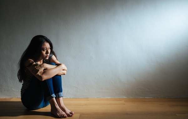 Испуганная девушка азиатка сидит у стены