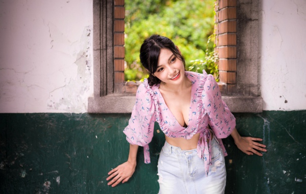 Улыбающаяся девушка азиатка стоит у окна 