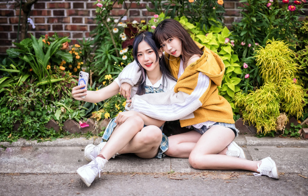 Две девушки азиатки сидят у стены с цветами 