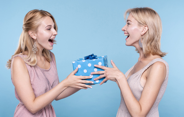 Две подруги блондинки с подарком на голубом фоне
