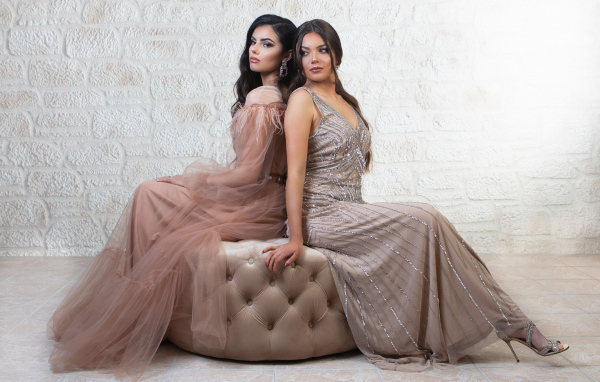 Две девушки в красивых платьях сидят на диване 