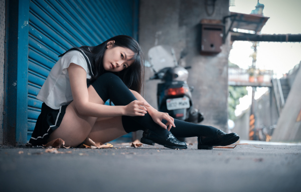 Молодая азиатка в черных чулках сидит у стены 