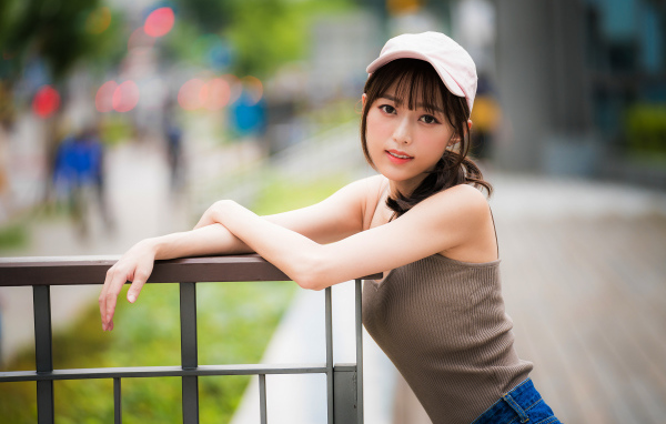 Молодая азиатка в кепке у перил 