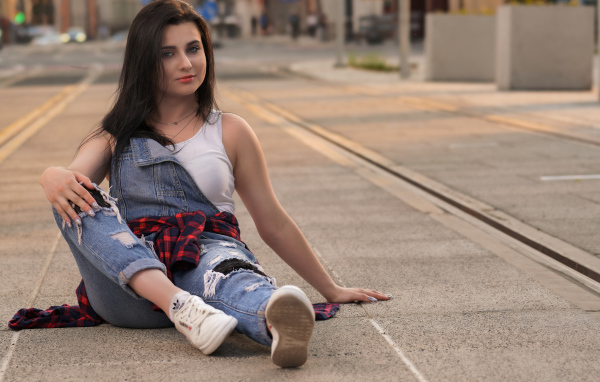 Молодая девушка в джинсовом наряде сидит на асфальте