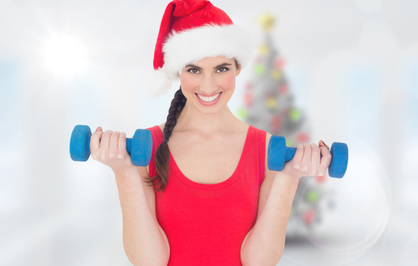 Красивая девушка в шапке Санта Клауса с гантелями в руках 